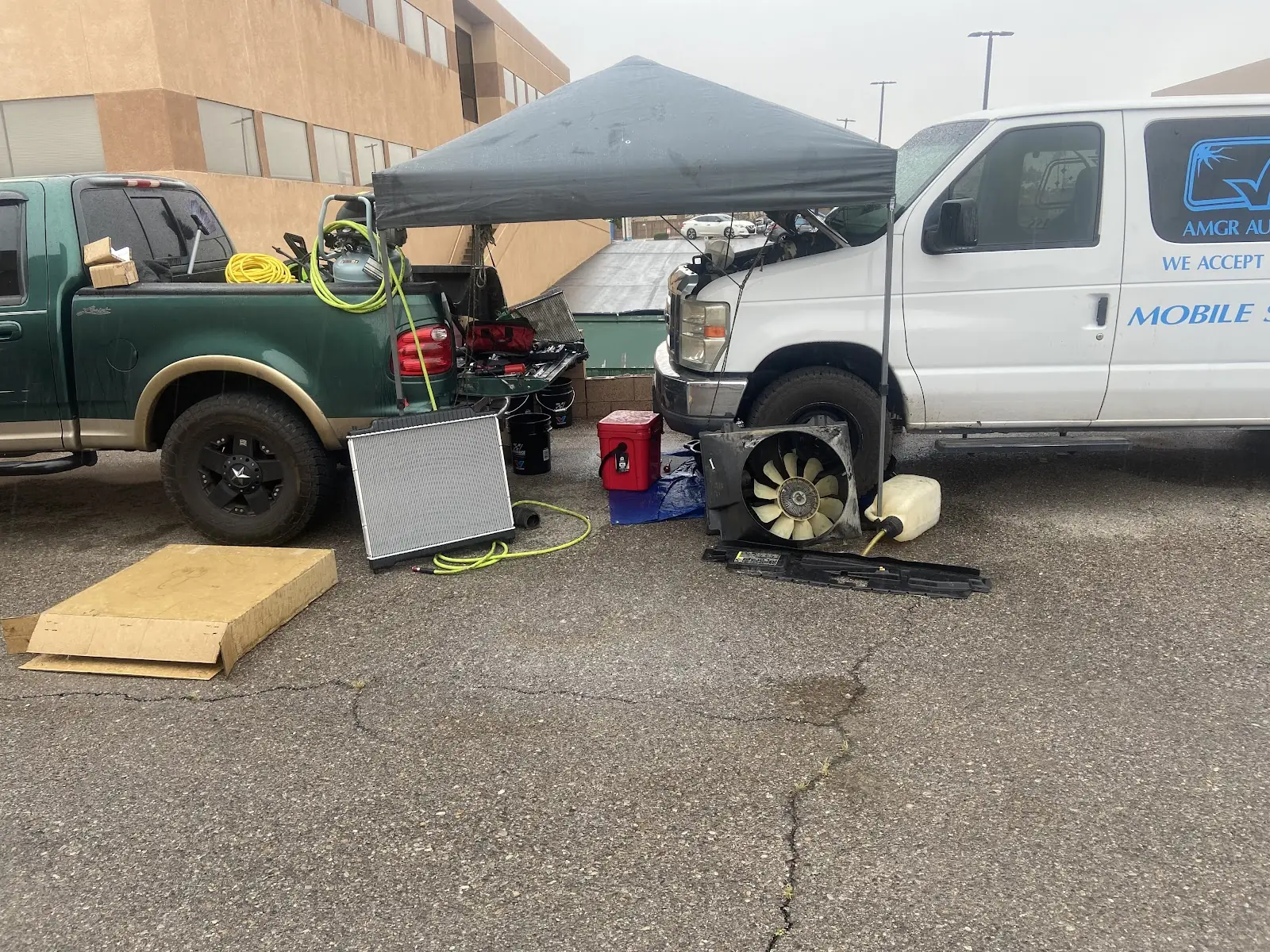 Mobile work site with a canopy, a work truck, a van with the hood up, and a radiator standing on the ground
