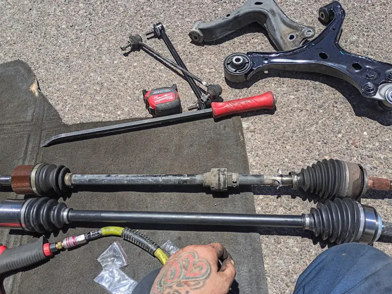Two CV axles, a control arm, and tools laid out on the pavement
