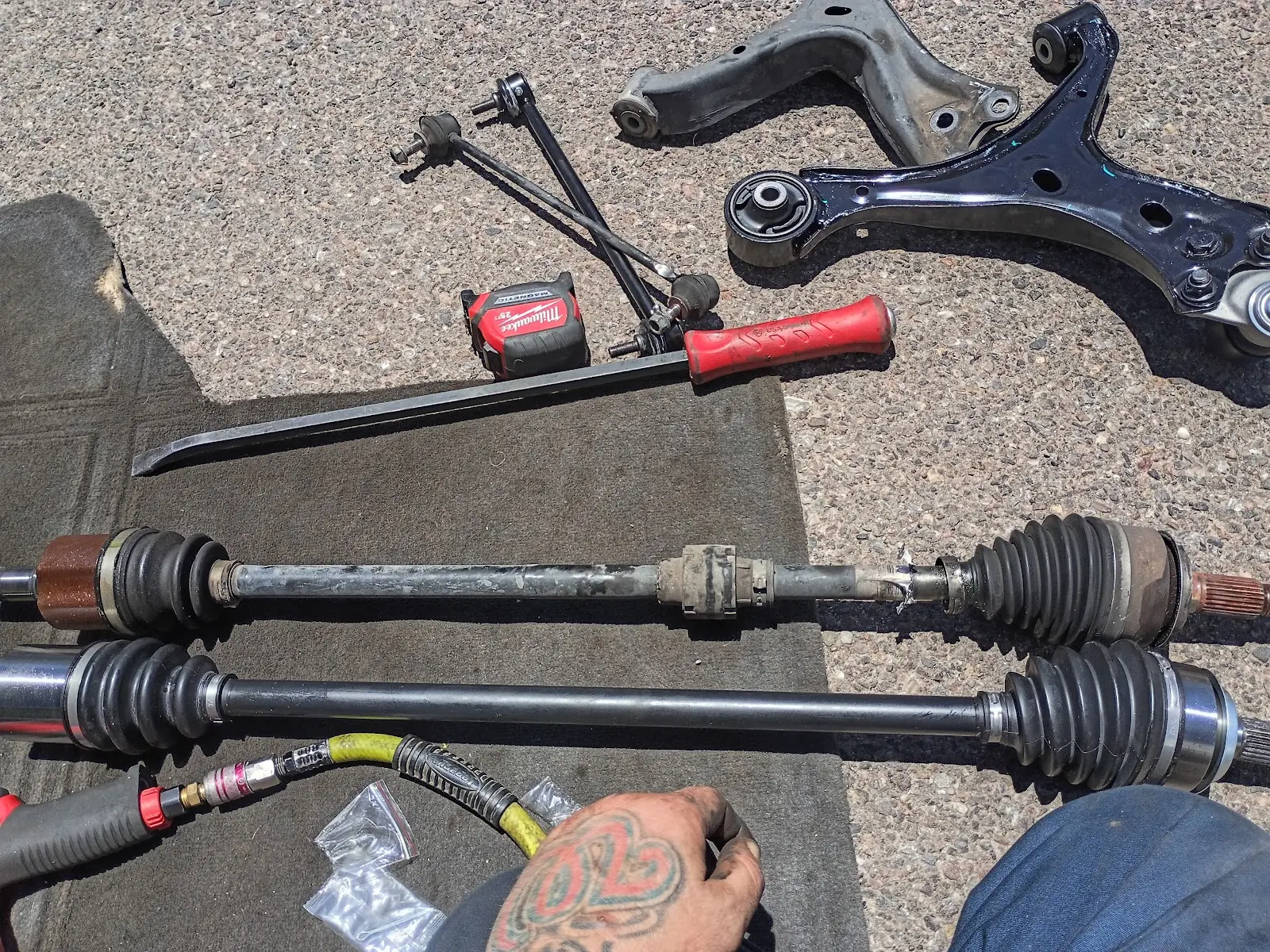 Two CV axles, a control arm, and tools laid out on the pavement