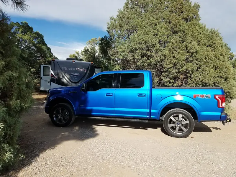 Blue Ford F-150 FX4 parked on a gravel driveway beside a travel trailer
